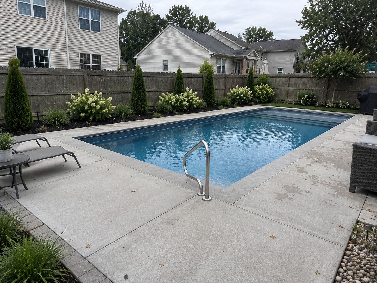 Modern backyard swimming pool with clear water, surrounded by landscaping and lounge chairs.