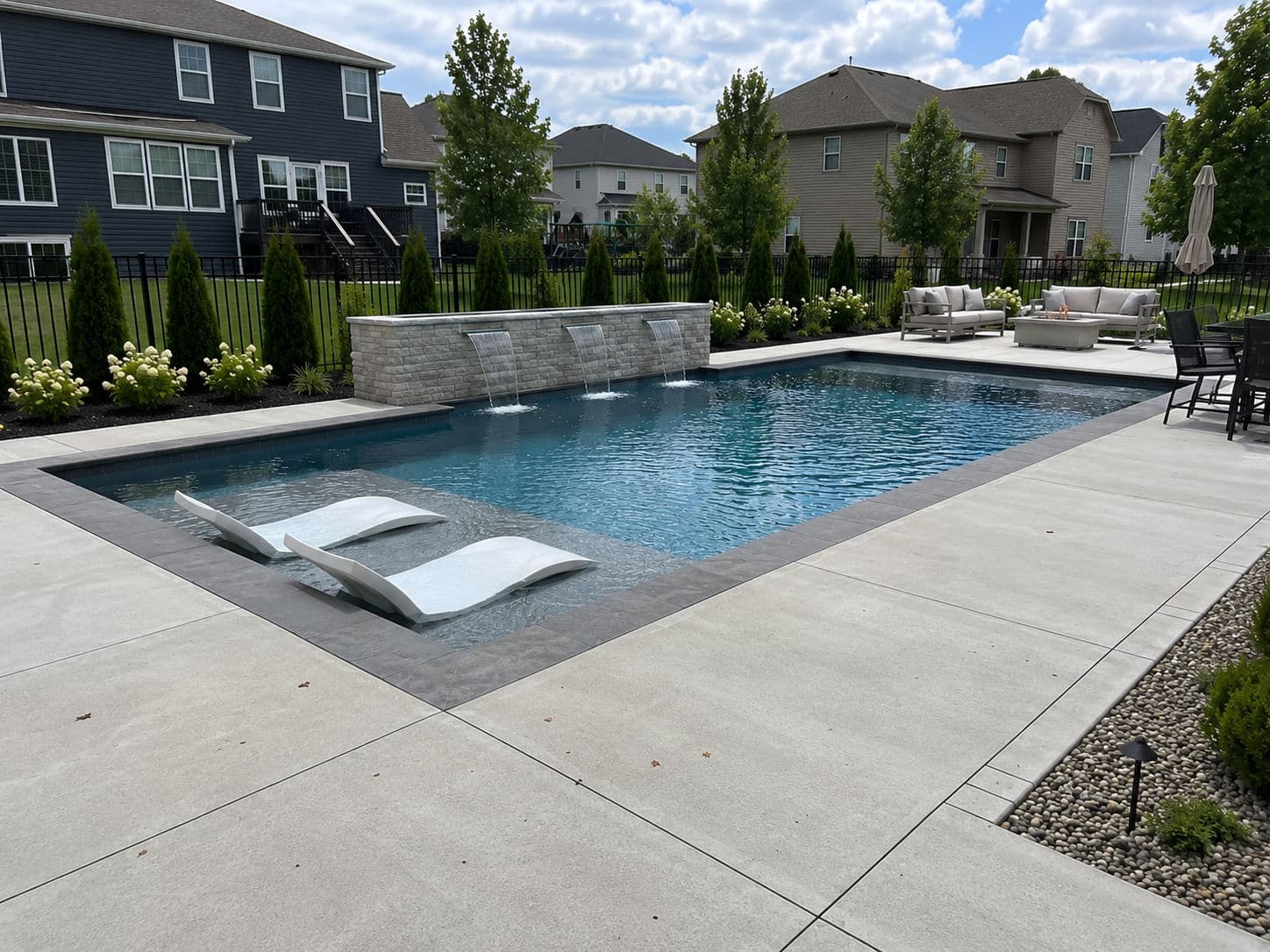 Luxury backyard pool with modern loungers, stone features, and landscaped greenery.
